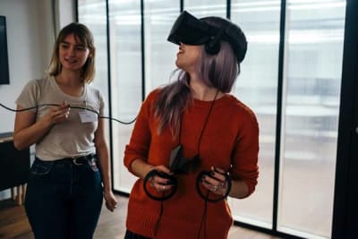 Girl with VR head-mounted display and controllers in her hands and girl holding wire