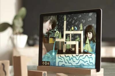 Tablet mirroring kids playing game KOSKI, enhanced with imaginative plants, figures and waterfall