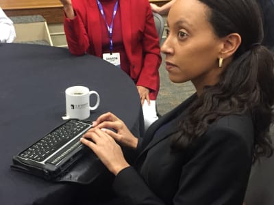 Haben Girma sits at a conference table and uses her braille reader.