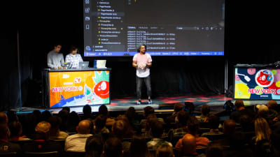 A photo of Dan Mall standing on stage explaining code shown on the screen behind him